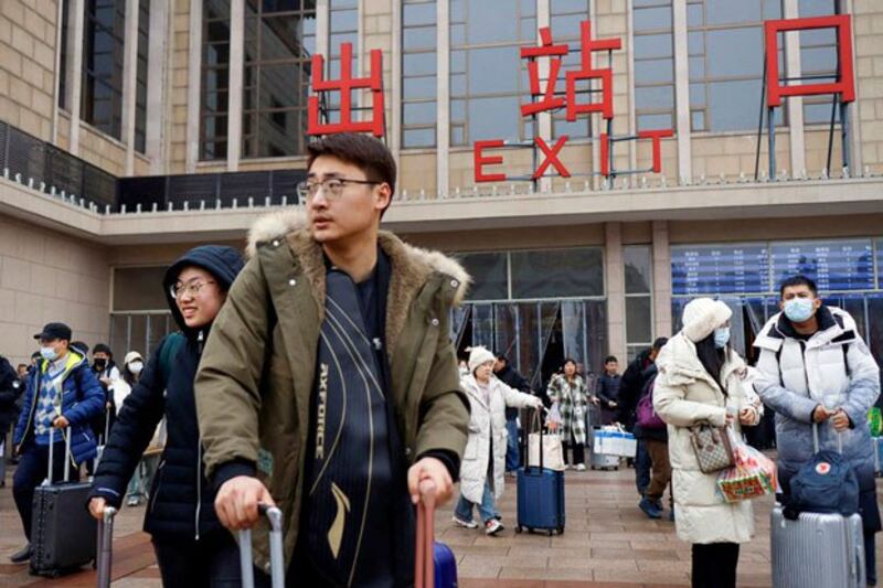 Travelers walk with their luggage outside the Beijing railway station in Beijing, China, Feb. 18, 2024. (Florence Lo/Reuters)