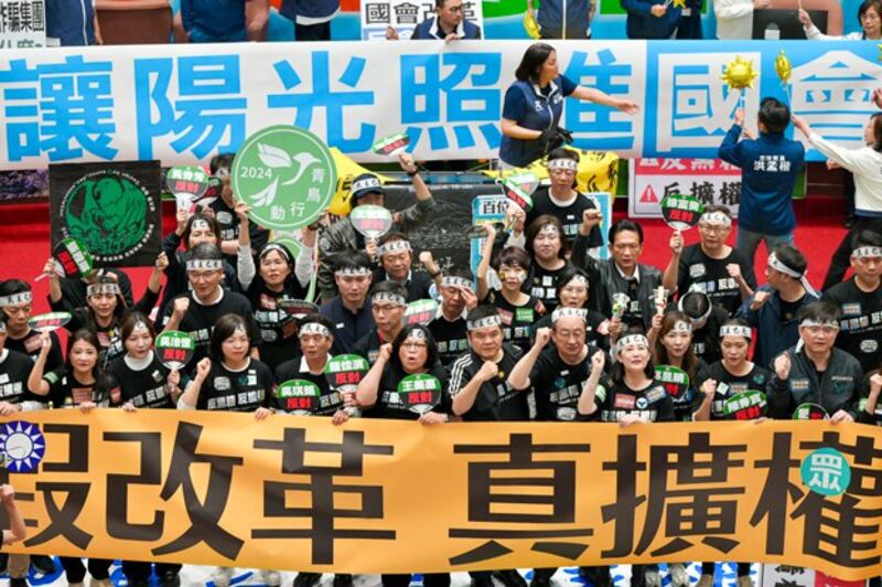 Lawmakers (bottom) from Taiwan's ruling Democratic Progressive Party display a banner reading 'False reform, true expansion of power,' as main opposition Kuomintang legislators unveil a banner reading 'Let sunshine light into Parliament' while voting for a controversial reform bill in Taipei, May 28, 2024. (Sam Yeh/AFP)