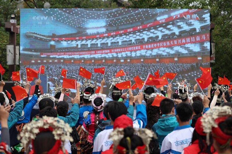 Ethnic minority members wave national flags as they watch the opening session of the 20th Chinese Communist Party Congress on a screen in Danzhai, in Chinaís southwestern Guizhou province, Oct. 16, 2022. Credit: AFP