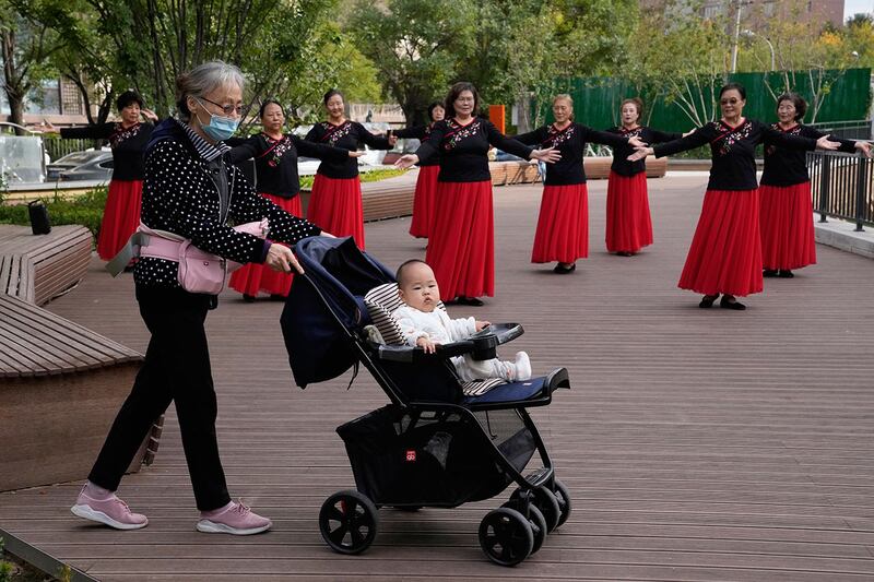 2021 年 10 月 14 日,一名老妇人推着婴儿车经过北京一公园的广场舞者。(美联社)