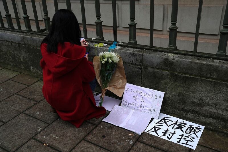 2022年11月28日,在中国驻伦敦大使馆外,一名妇女在写着“反核酸,反封控”的标语牌旁边点着蜡烛。(美联社)