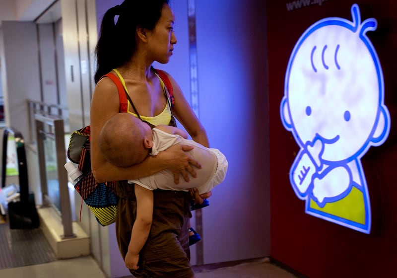 图为,一名携带婴儿的妇女,在北京购物中心的婴儿卡通标志前。 (美联社)