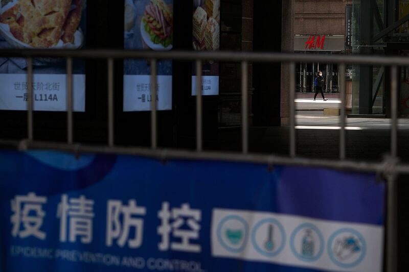 2022 年 5 月 12 日，在北京朝阳区，当局下令关闭非必要业务并要求人们在家工作后，一名戴着口罩的妇女走过关闭的商场。（美联社）