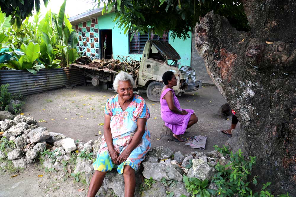 An older woman sits on a fence outside her house. People in villages around Port Vila live simply, often without basic necessities. Forty percent of the population lacks access to electricity.  Photo: RFA